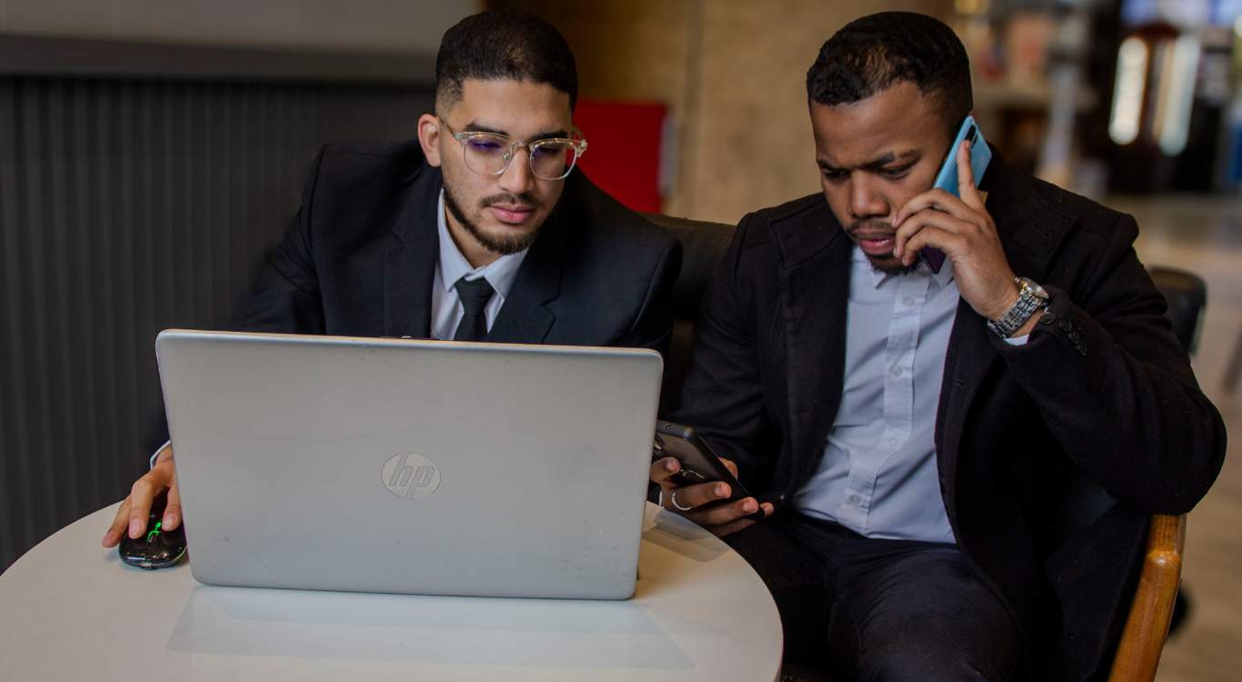 The co-founders of IDK Solutions working collaboratively in a local cafe, managing client operations via smartphone and laptop to demonstrate hands-on partnership.