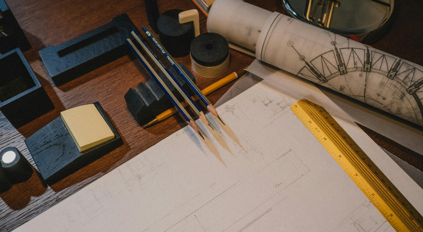 Close-up of architectural blueprints and drafting pencils on a wooden desk, symbolizing the precise and secure data privacy structure engineered by IDK Solutions.