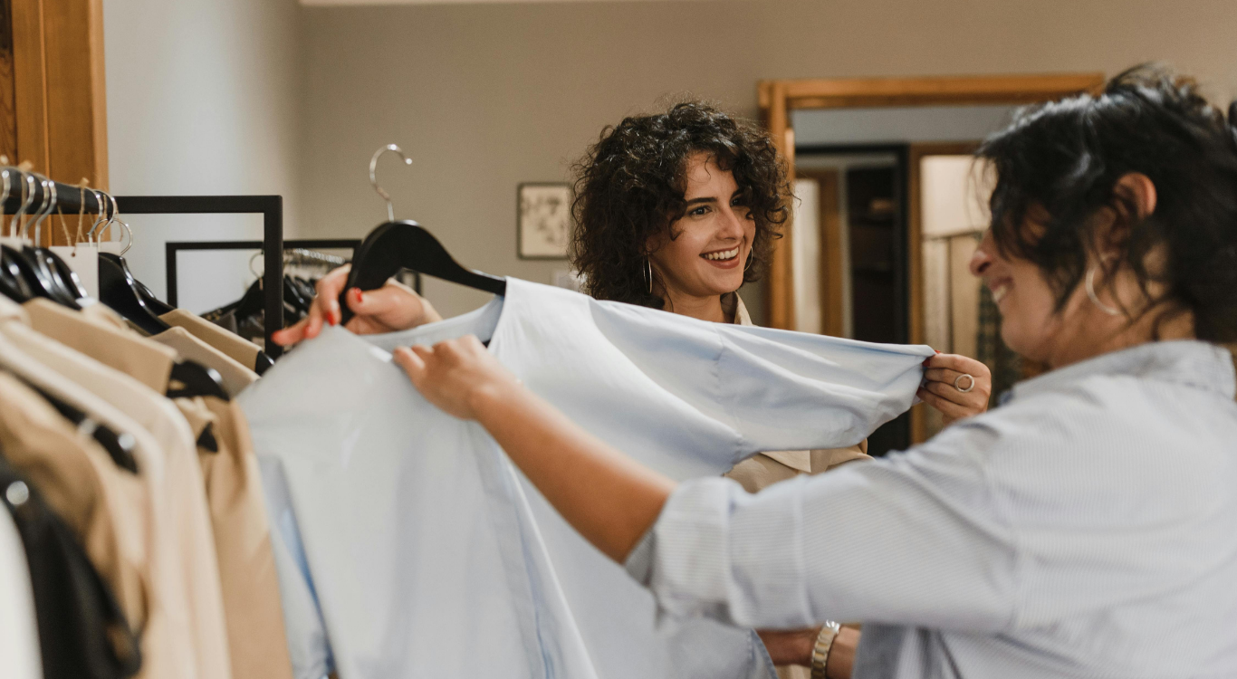 Two customers smiling while browsing clothes in a boutique, representing the seamless retail experience created by optimized digital operations.
