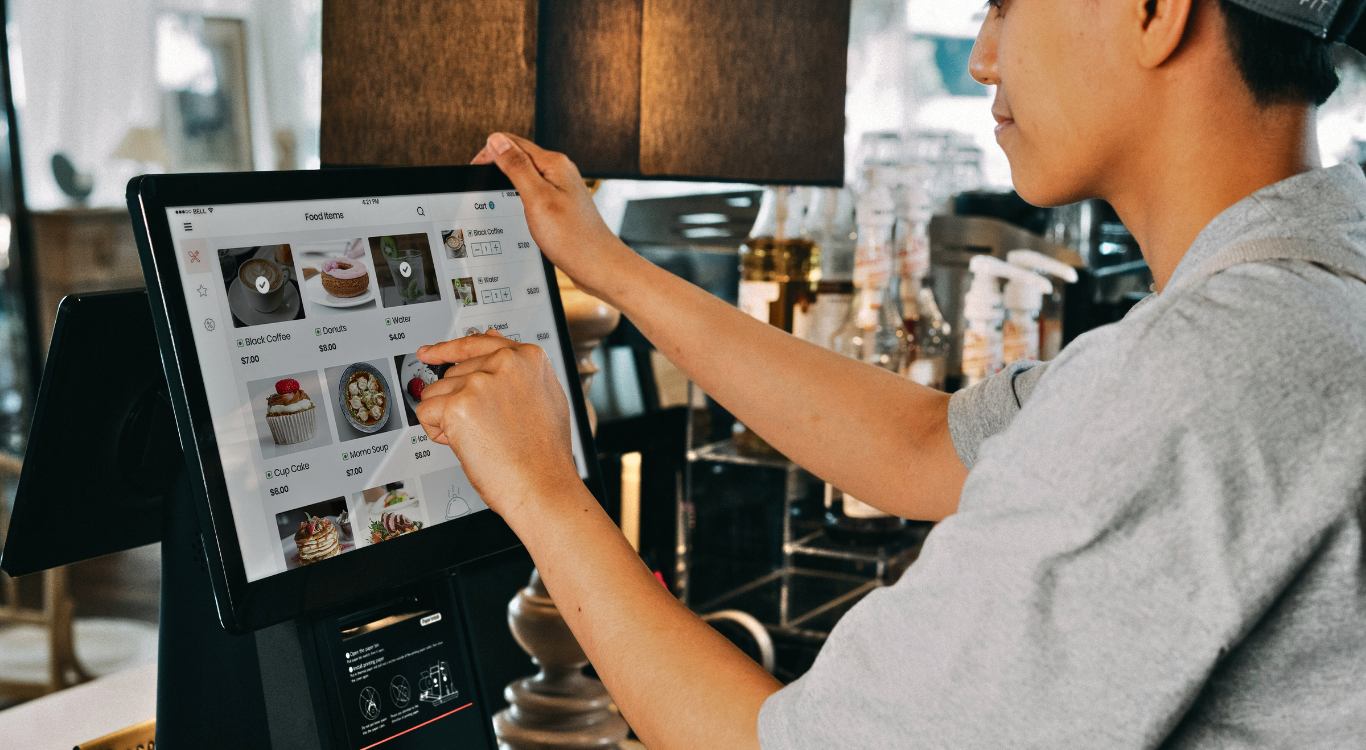 Cafe staff member using a digital touchscreen POS system, illustrating how custom software streamlines brick-and-mortar operations